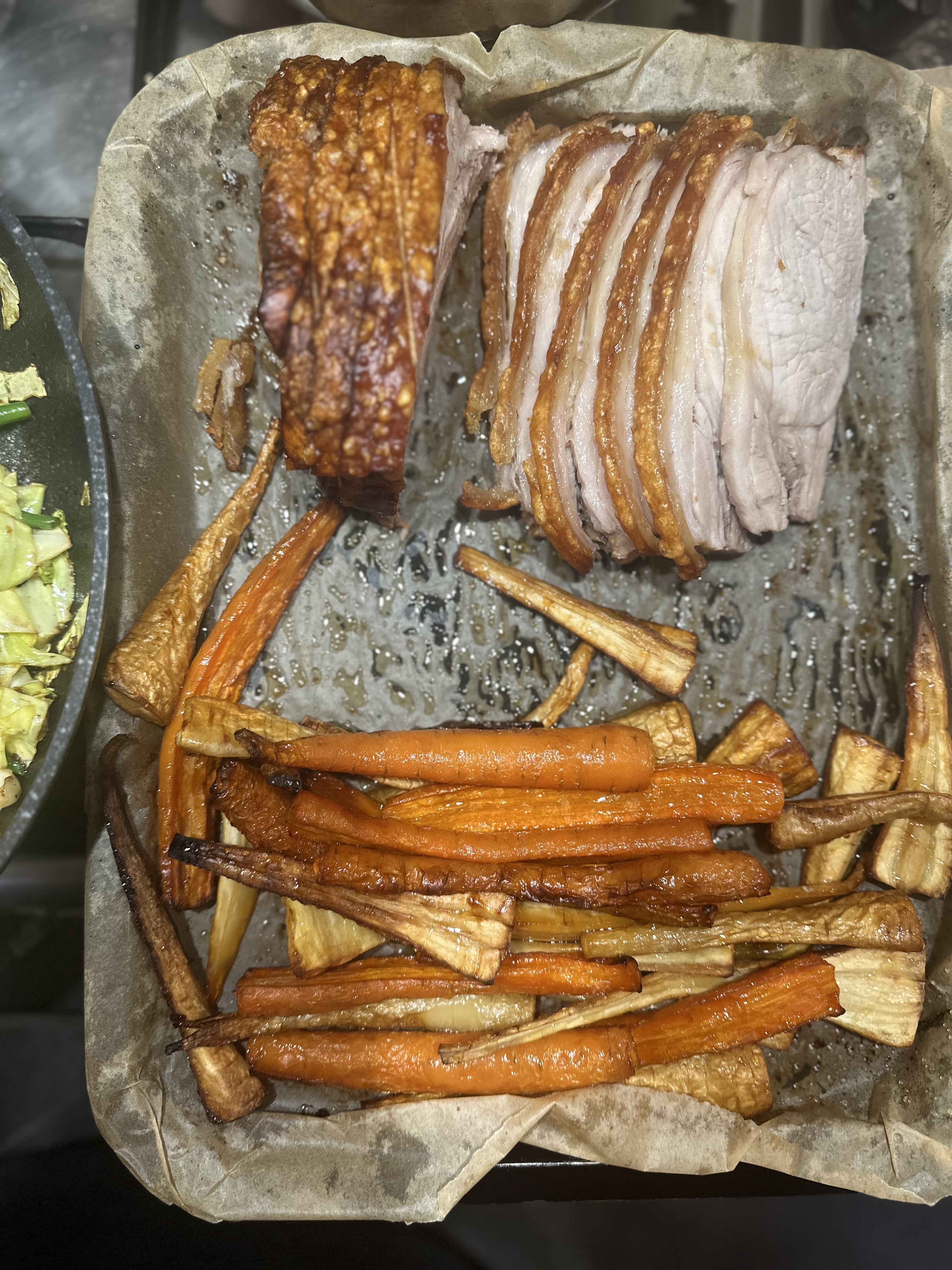 Succulent slices of roast pork with crispy crackling sit atop parchment, surrounded by golden roasted carrots and parsnips, exuding a cozy vibe.