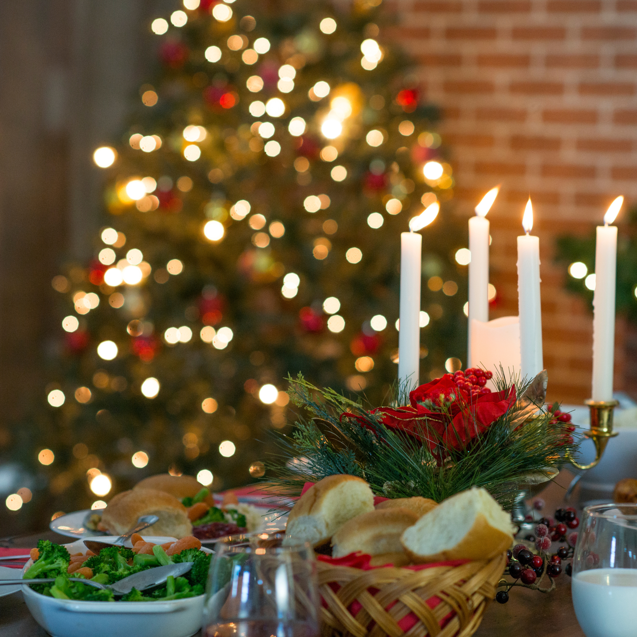 A festive table showcases crisp salads, rolls in a wicker basket, and elegant candlelight, all set against a twinkling Christmas tree.