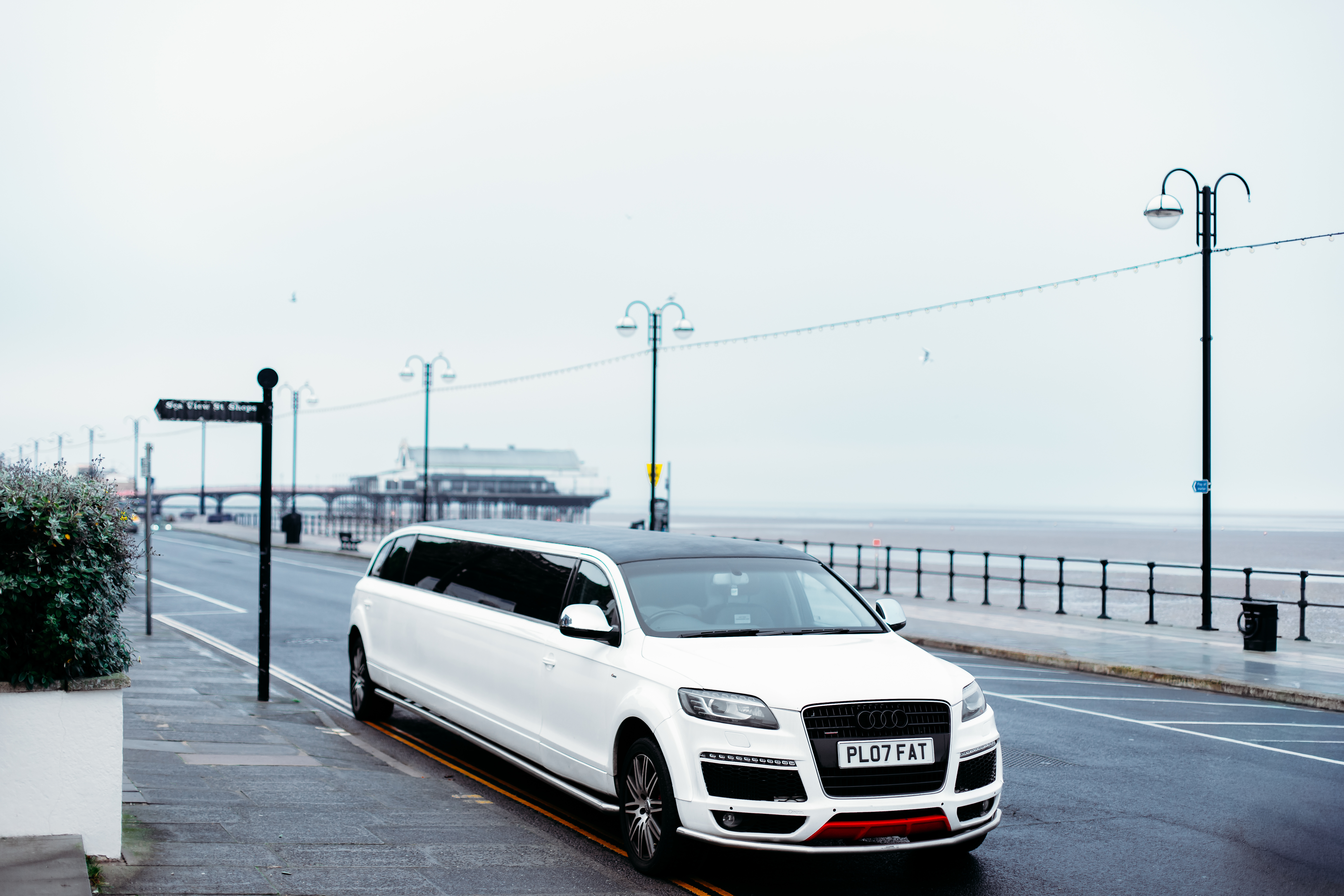 A sleek white limousine parked along a coastal road, showcasing wet pavement and muted gray skies, exudes luxury for your special occasion.