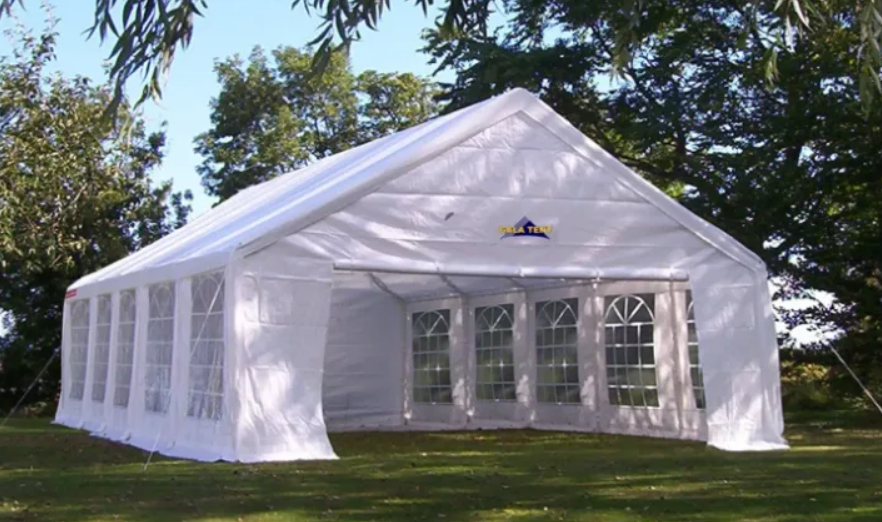 The spacious white tent, featuring large arched windows, is set against a vibrant green backdrop, ideal for an elegant outdoor event.