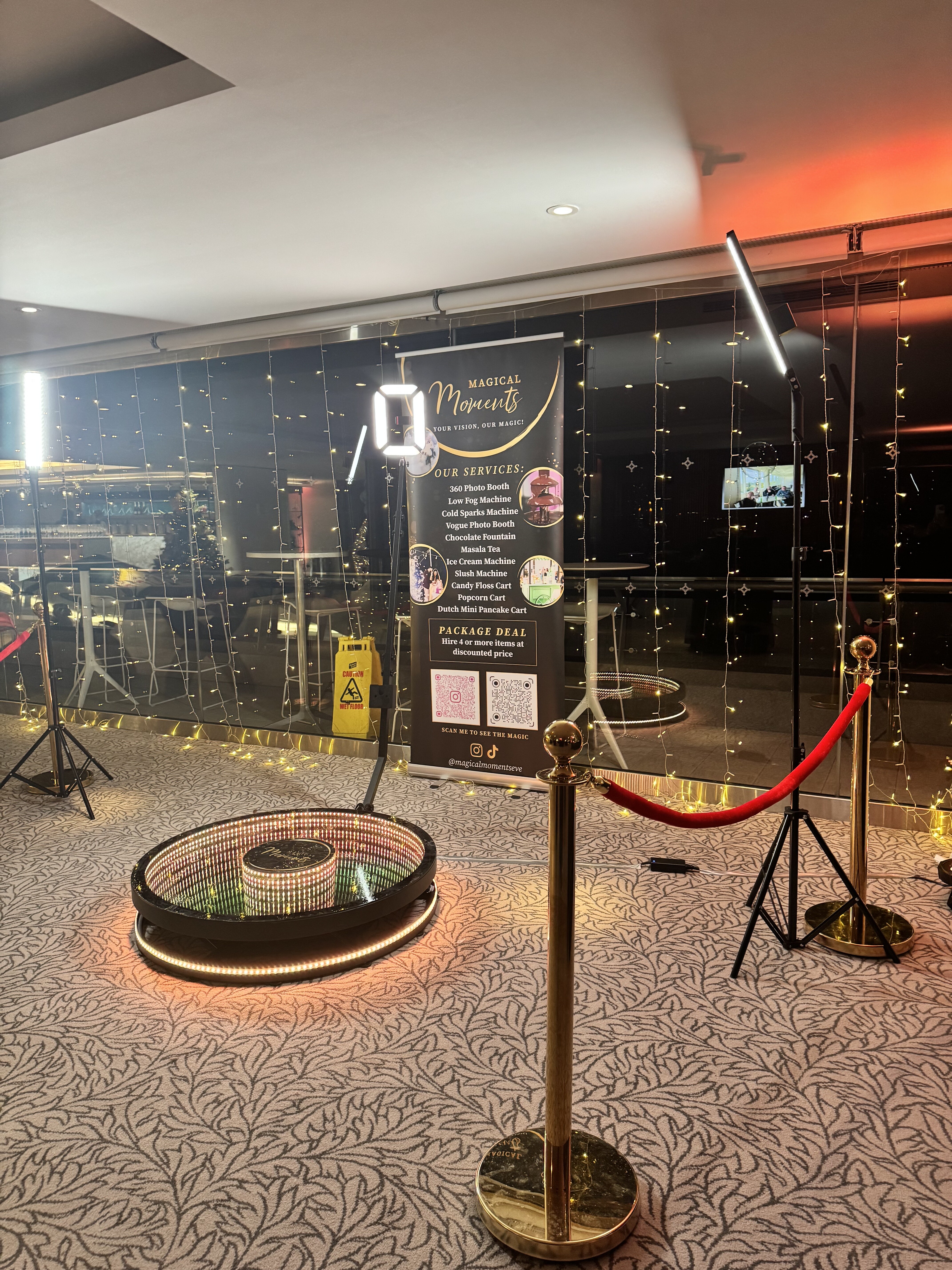 A chic event setup features a glowing circular photo booth with gold accents, a black backdrop, and twinkling fairy lights, creating a festive atmosphere.