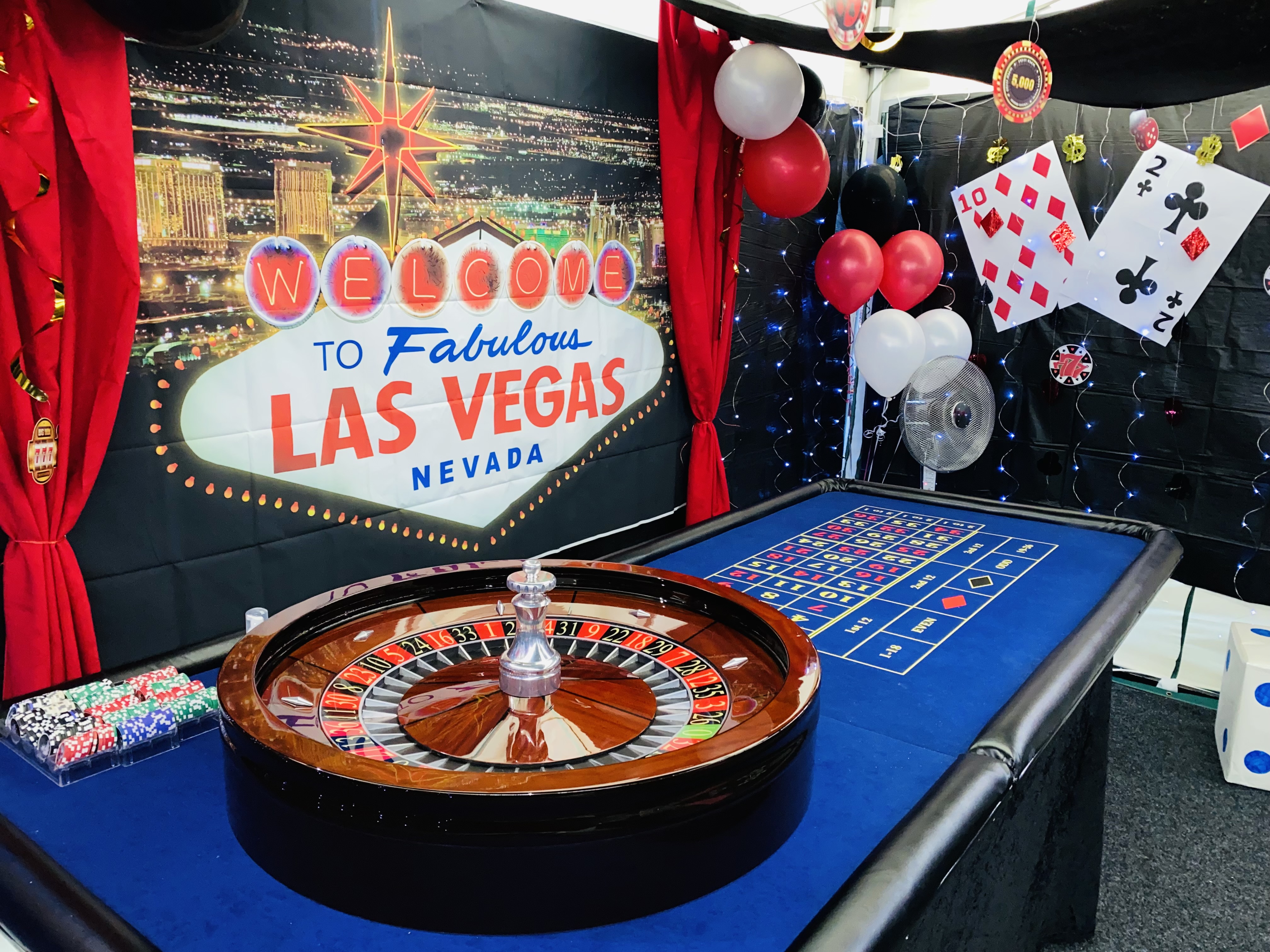 A vibrant Las Vegas-themed setup features a wooden roulette table, colorful chips, and dramatic black drapes, evoking a lively atmosphere.
