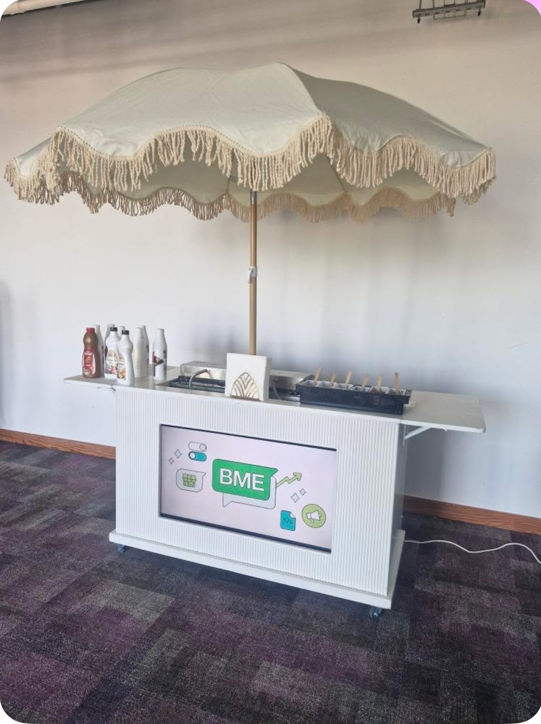 A charming service cart with a cream umbrella featuring fringes showcases assorted condiments and sauces, perfect for catering events.