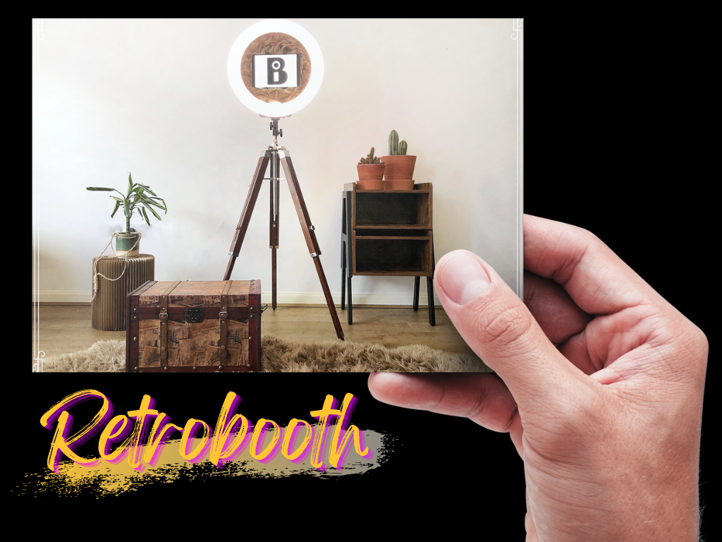 A wooden vintage trunk sits on a soft rug, illuminated by a bright ring light on a tall tripod, with a potted plant nearby, creating a cozy photo booth vibe.