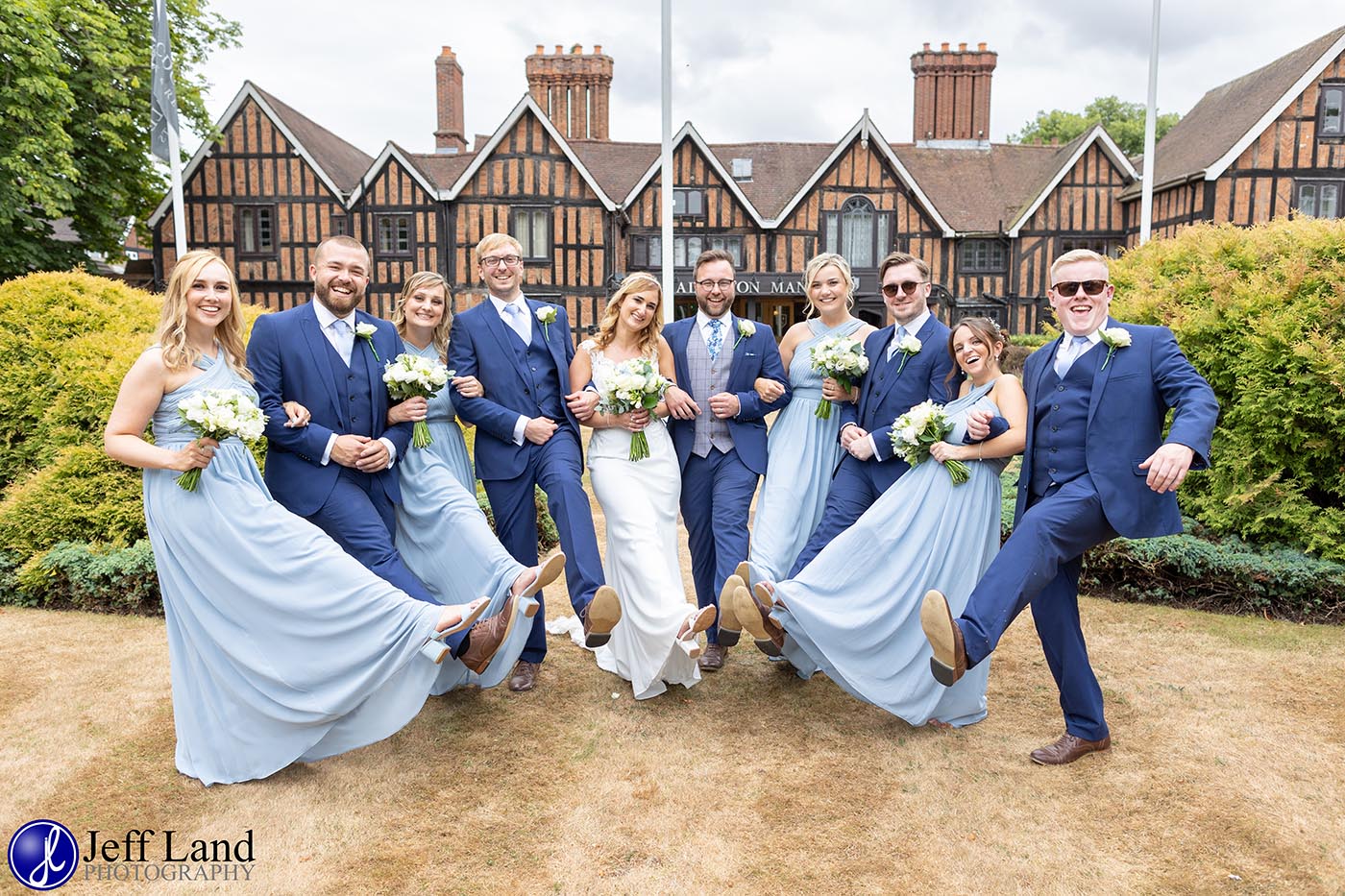 A cheerful wedding party, dressed in light blue outfits, showcases bouquets against a charming heritage venue with a lively atmosphere.