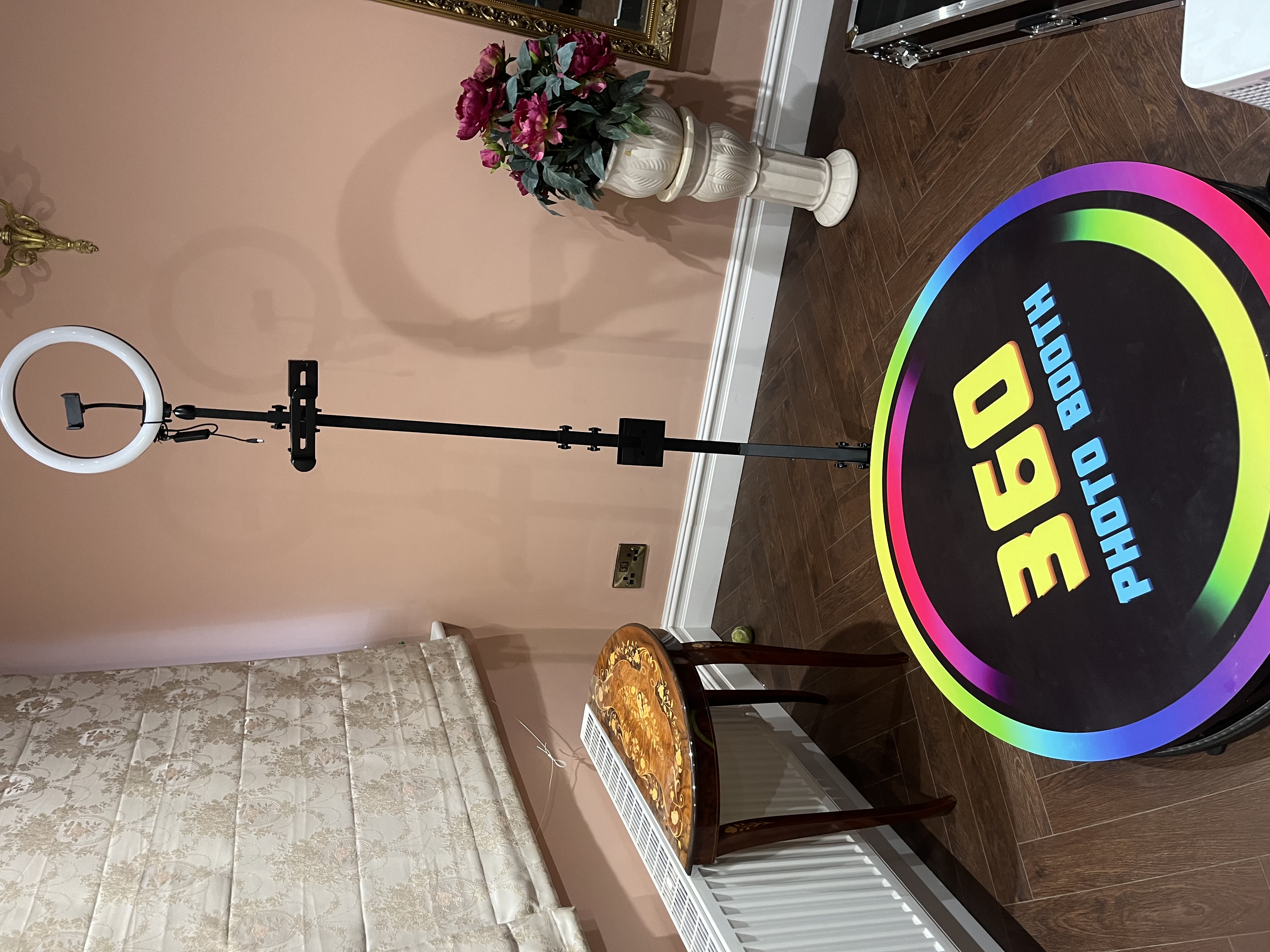 A modern 360 photo booth with vibrant rainbow accents is set against soft pink walls, basked in warm ambient lighting, perfect for events.