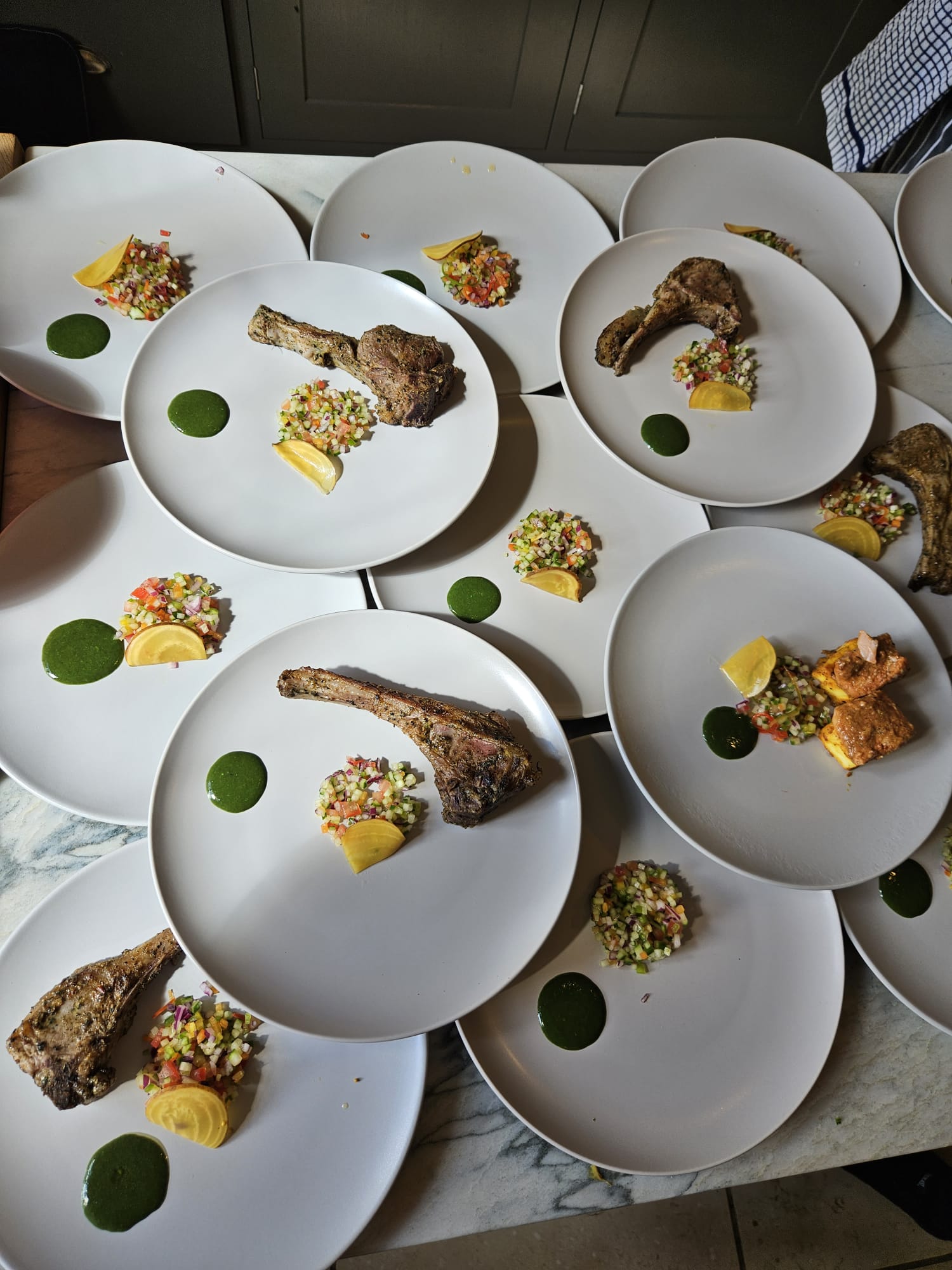 Elegant white plates host perfectly cooked lamb chops, vibrant salsa, lemon wedges, and herb sauce, creating a gourmet buffet display.