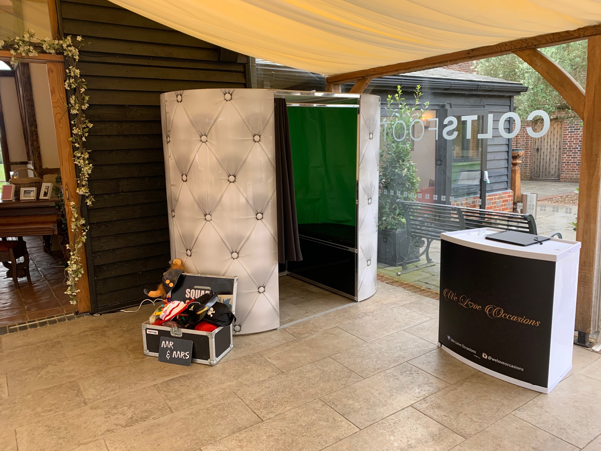 A stylish photo booth with a sleek, tufted exterior sits on light stone flooring, beside a display of fun props, creating a lively atmosphere.
