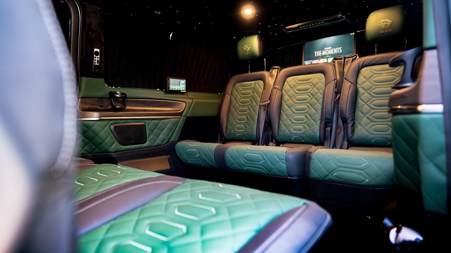 Luxurious leather seats in rich green and brown tones are arranged in a spacious, sleek vehicle interior, creating an upscale vibe.