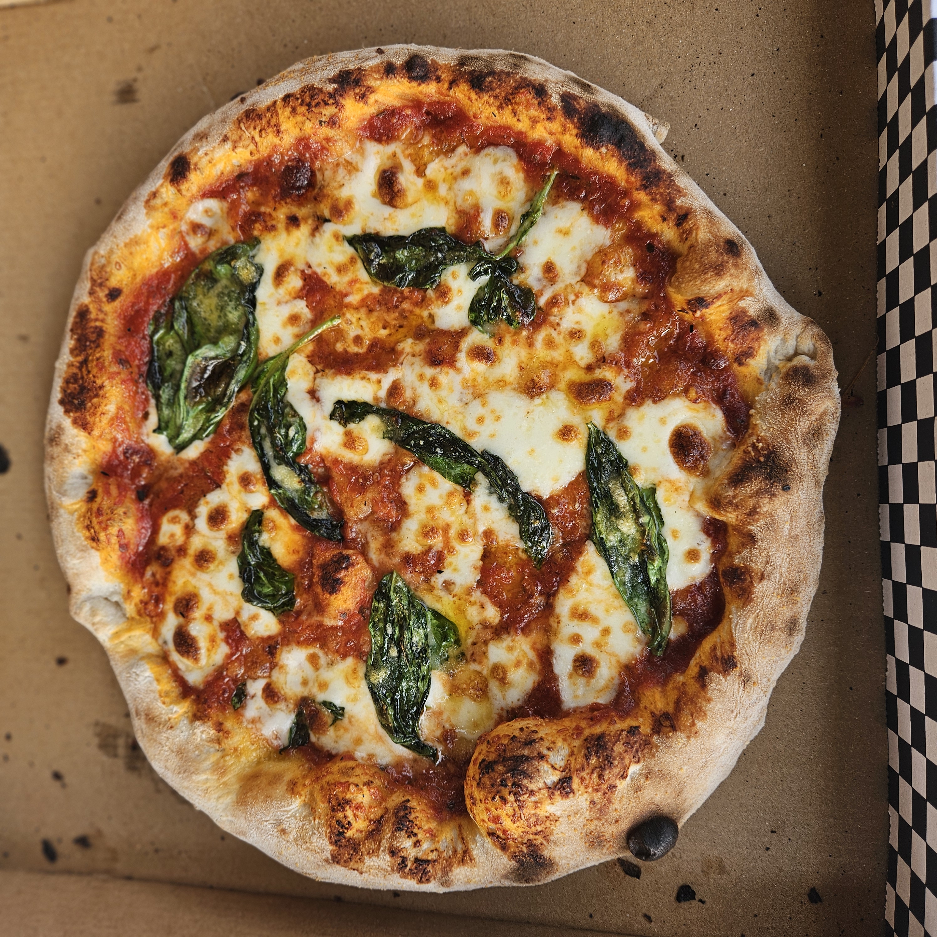 Artisan Margherita pizza with basil and melted mozzarella, nestled in a rustic box, warm wood-fired catering presentation, crisp and appetizing.