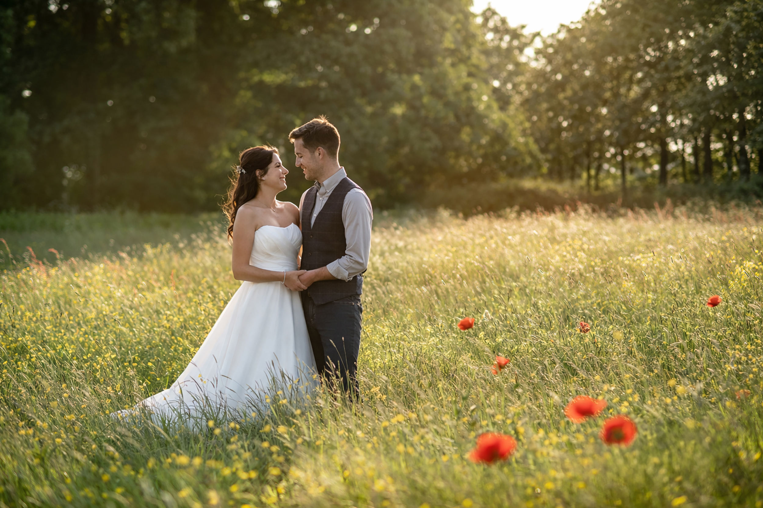 A couple stands in a sunlit field, surrounded by wildflowers and bright red poppies, exuding romance in a serene, natural setting.