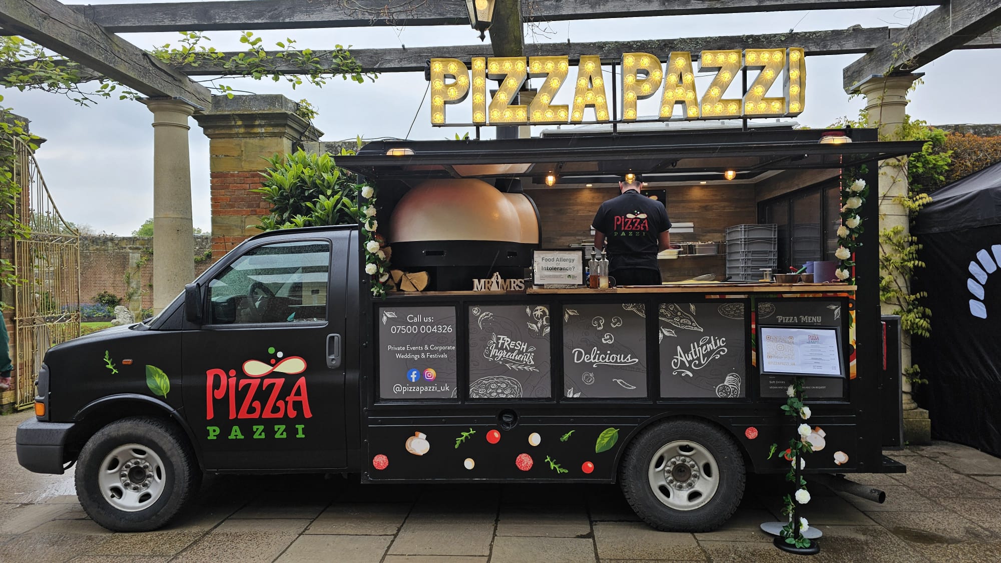 A pizza truck, adorned with fresh ingredients graphics, offers a cozy atmosphere under overcast skies, showcasing vibrant colors and thoughtful decor.
