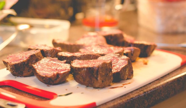 Juicy, perfectly seared beef cuts arranged on a red-trimmed cutting board, glistening under warm kitchen lighting, showcase quality catering.