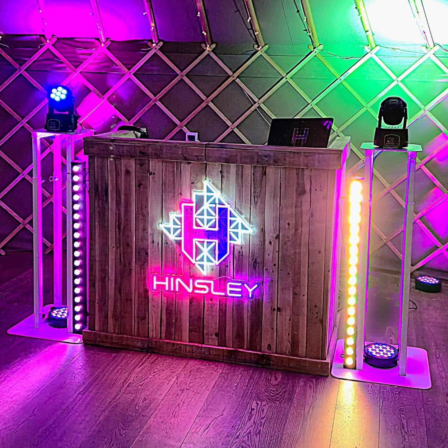 A rustic wooden bar showcases vibrant neon signage, illuminated by colorful stage lights, creating a lively, modern atmosphere perfect for events.