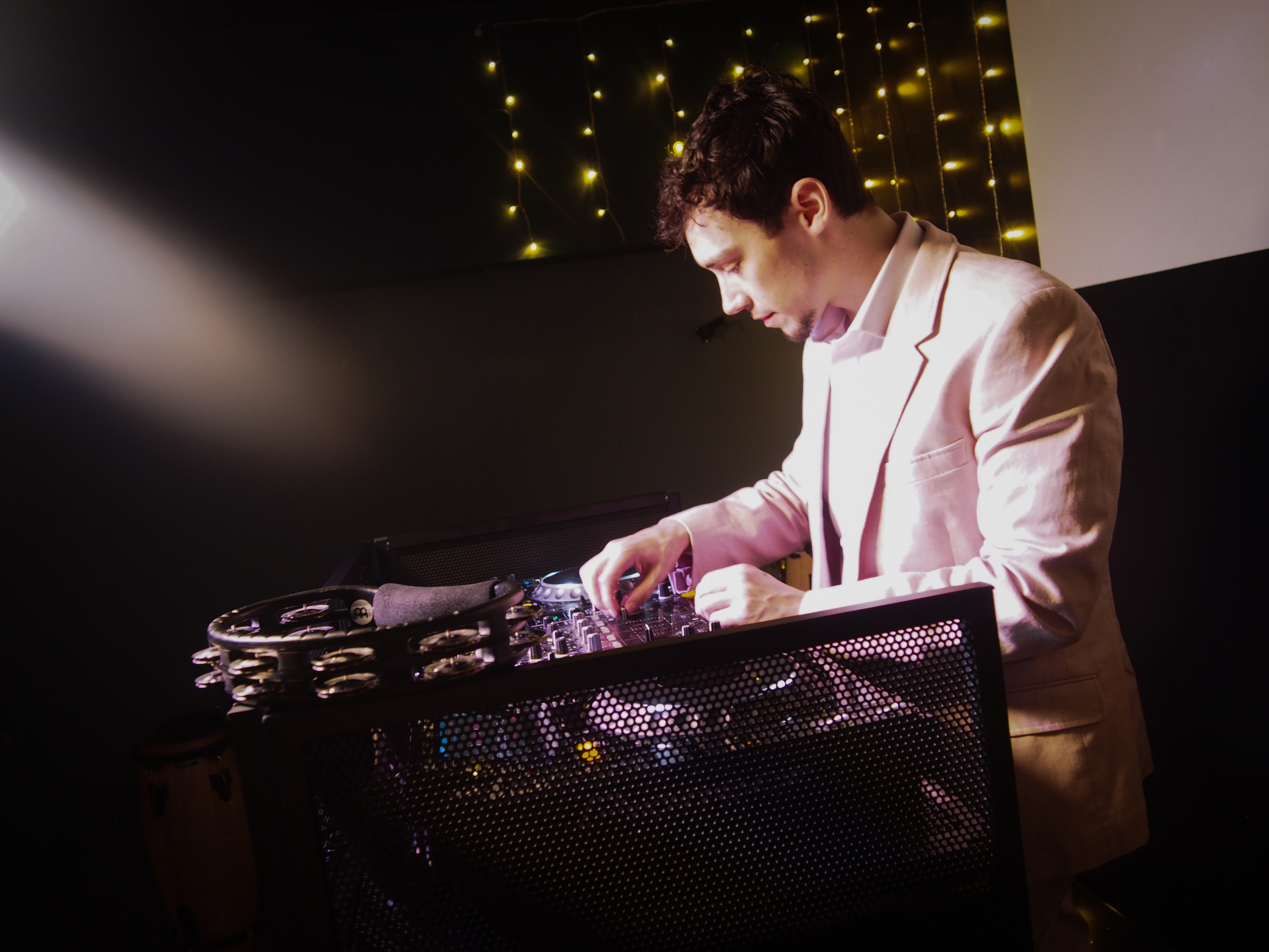 A DJ in a light pink suit meticulously adjusts a mixer under soft, warm lighting, creating an inviting atmosphere for events.