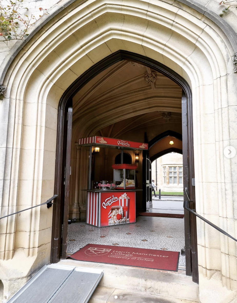 Red popcorn and candy stall in a Gothic stone archway, with polished service counter, warm indoor lighting, and Harris Manchester mat.