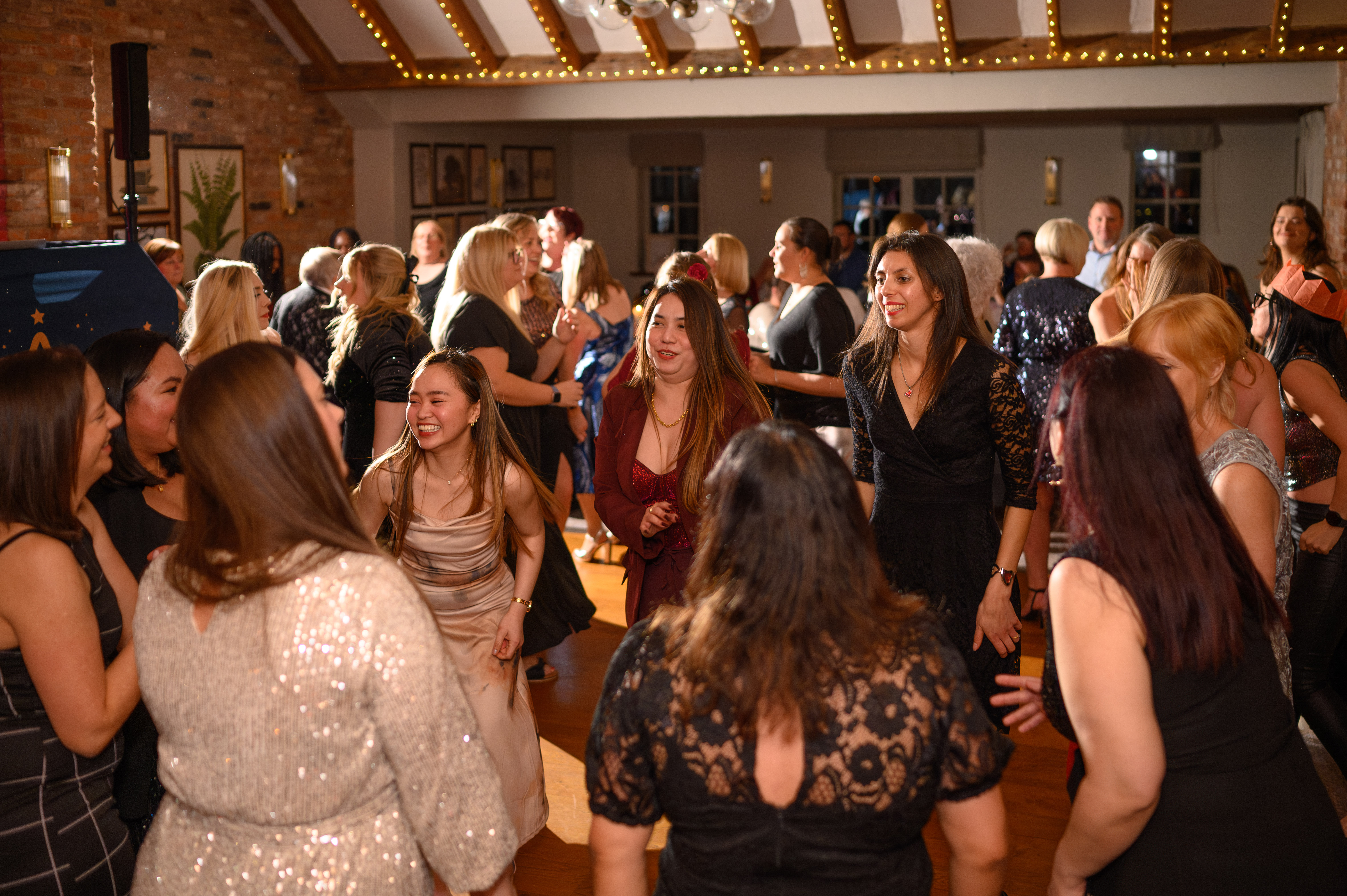 A lively crowd dances under warm, twinkling lights, showcasing elegant outfits with sequins and lace, creating a festive, vibrant atmosphere.