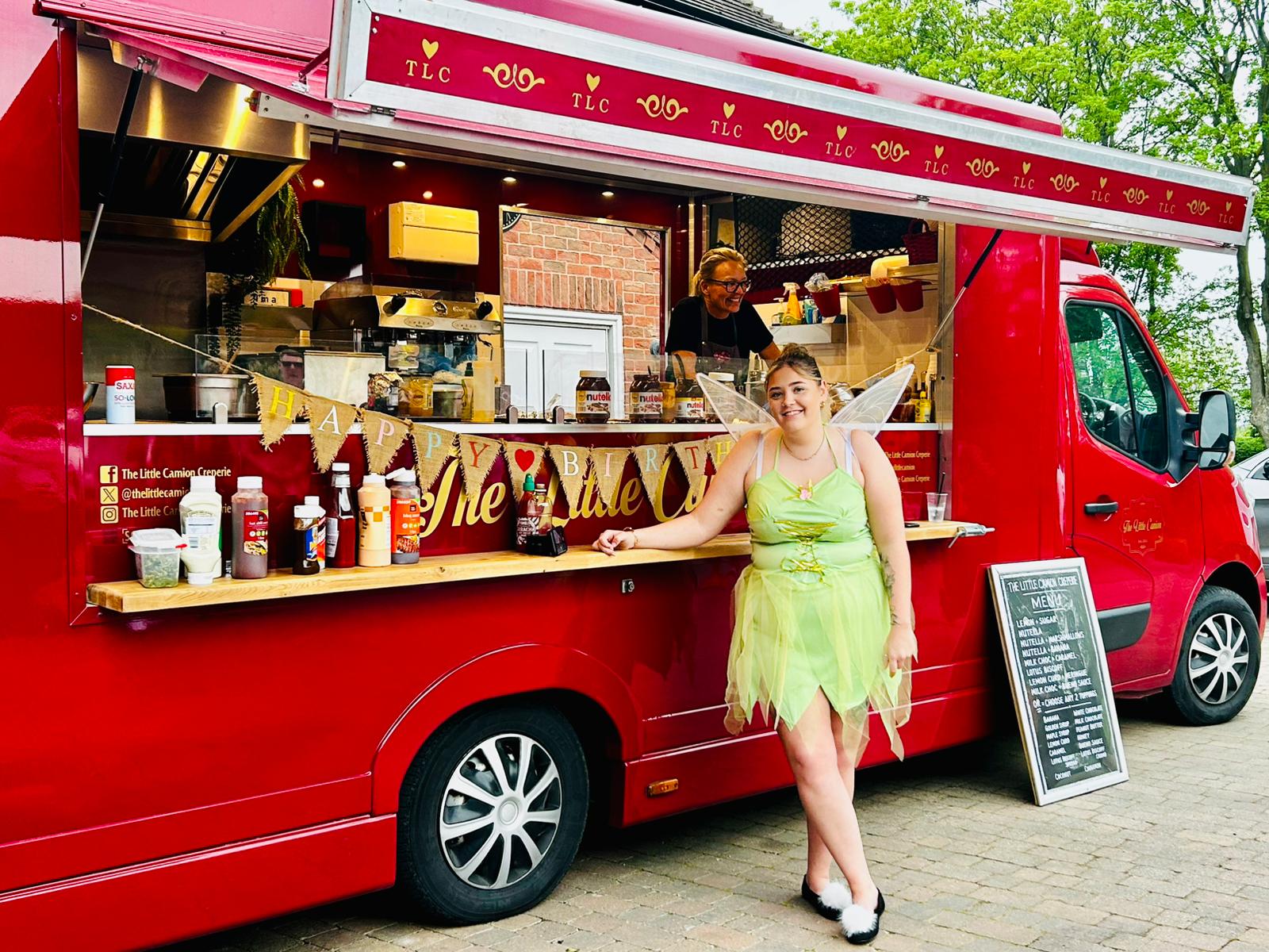 A vintage food truck with maroon and white colors features friendly staff in matching outfits, showcasing a colorful menu and condiments.