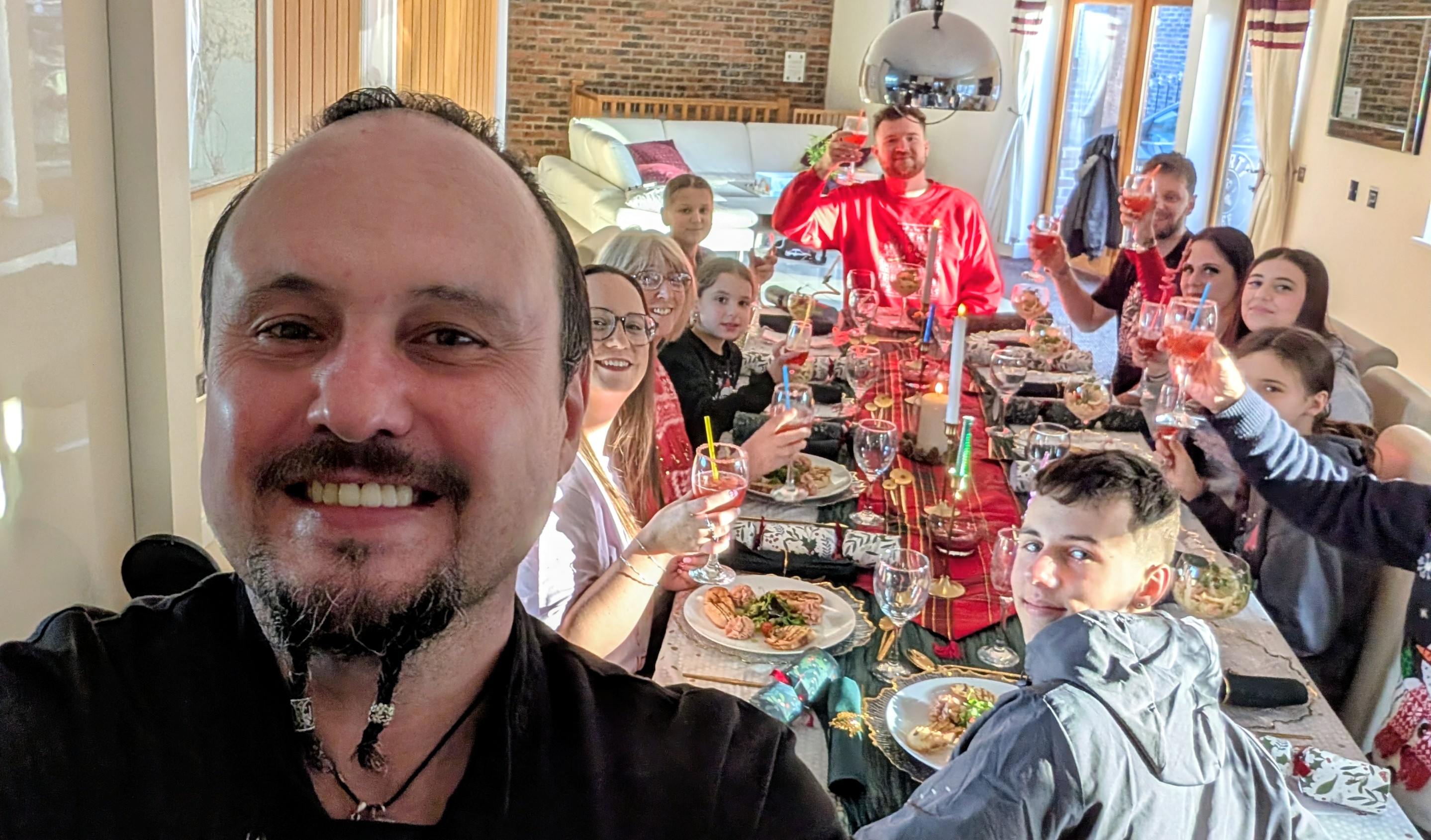 A festive gathering features a long table adorned with vibrant tablecloths, sparkling glassware, and family members raising drinks in cheer, bathed in warm light.