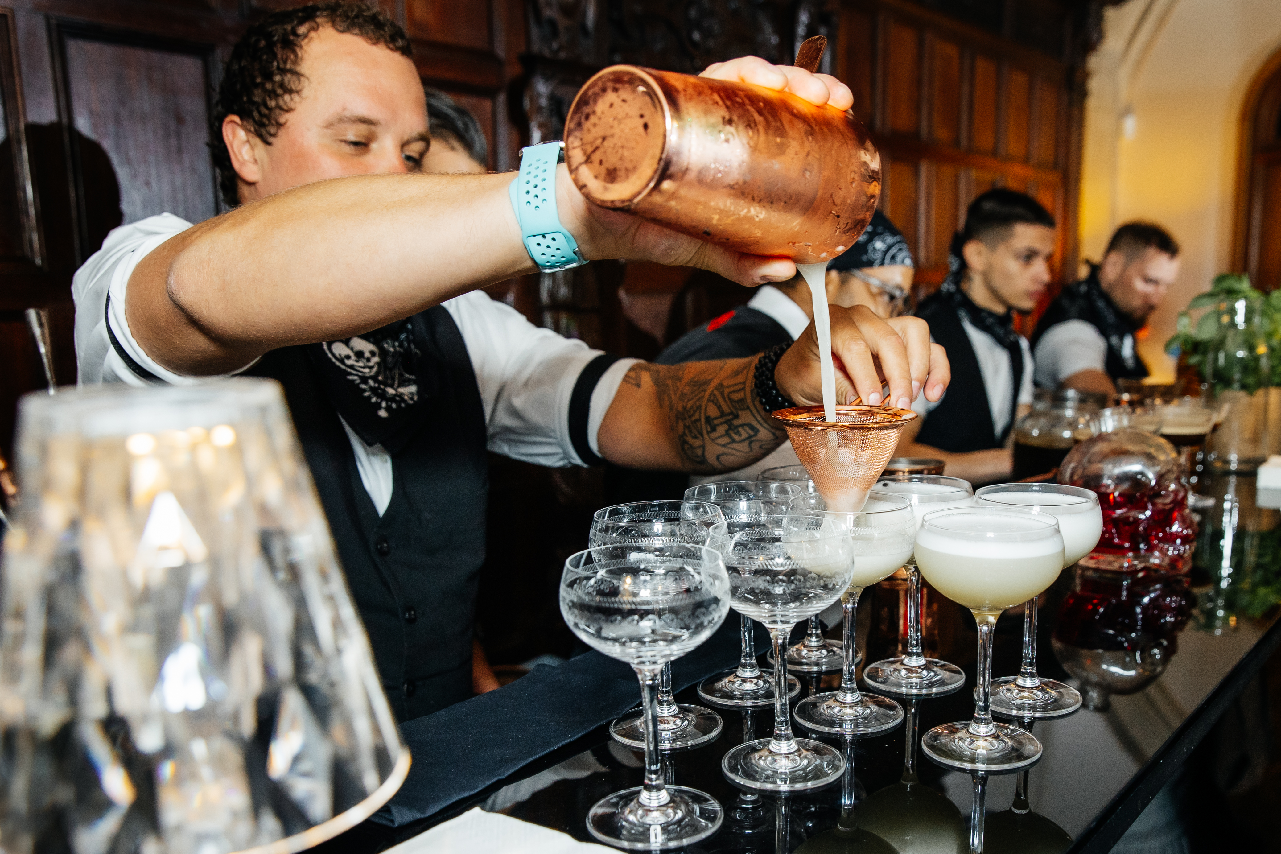 Skilled bartenders in tailored vests mix cocktails with precision into elegant glassware on a polished black bar, creating a vibrant atmosphere.