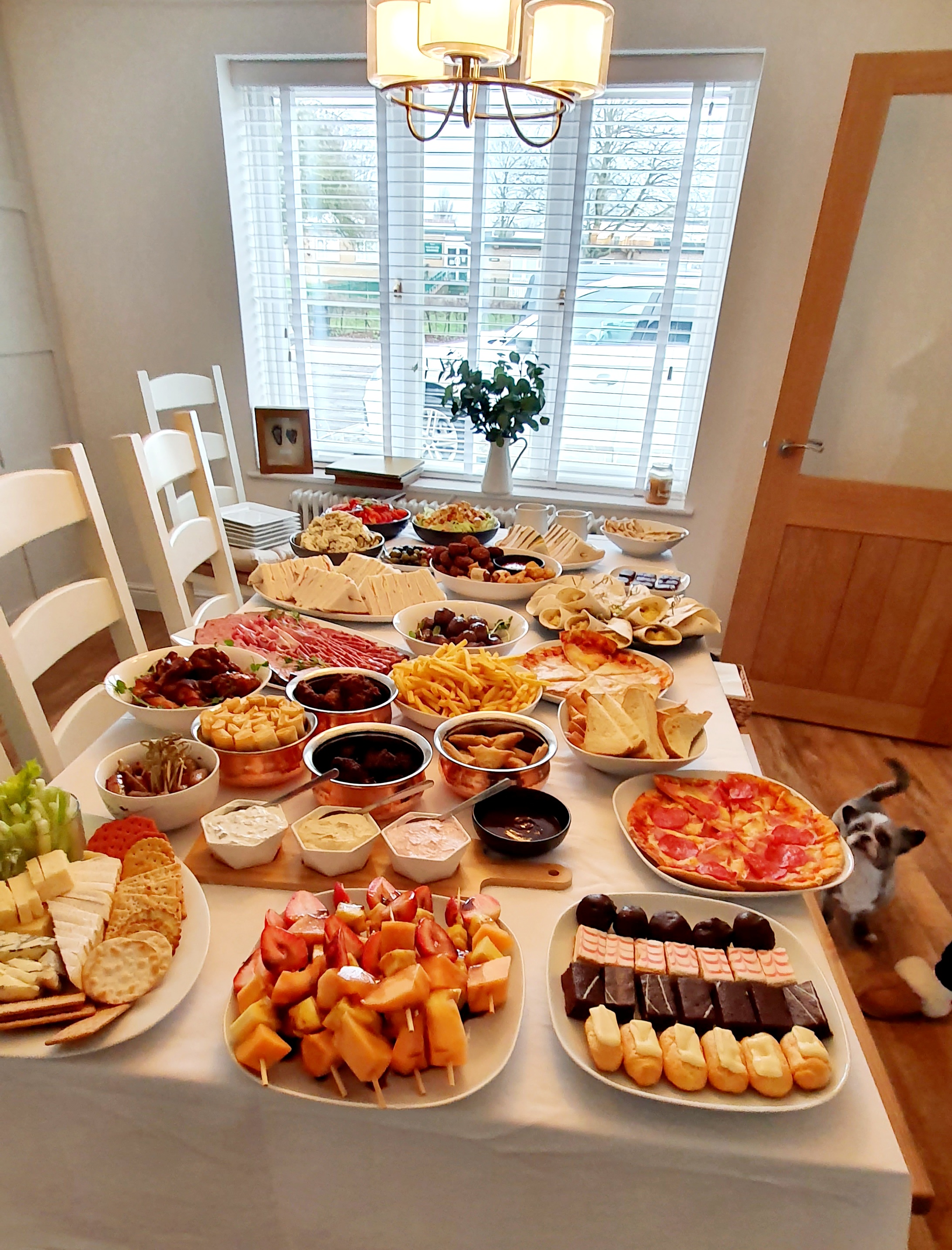 A vibrant buffet spreads across a white table, featuring assorted cheeses, fruits, and crispy snacks, all under warm, inviting light.