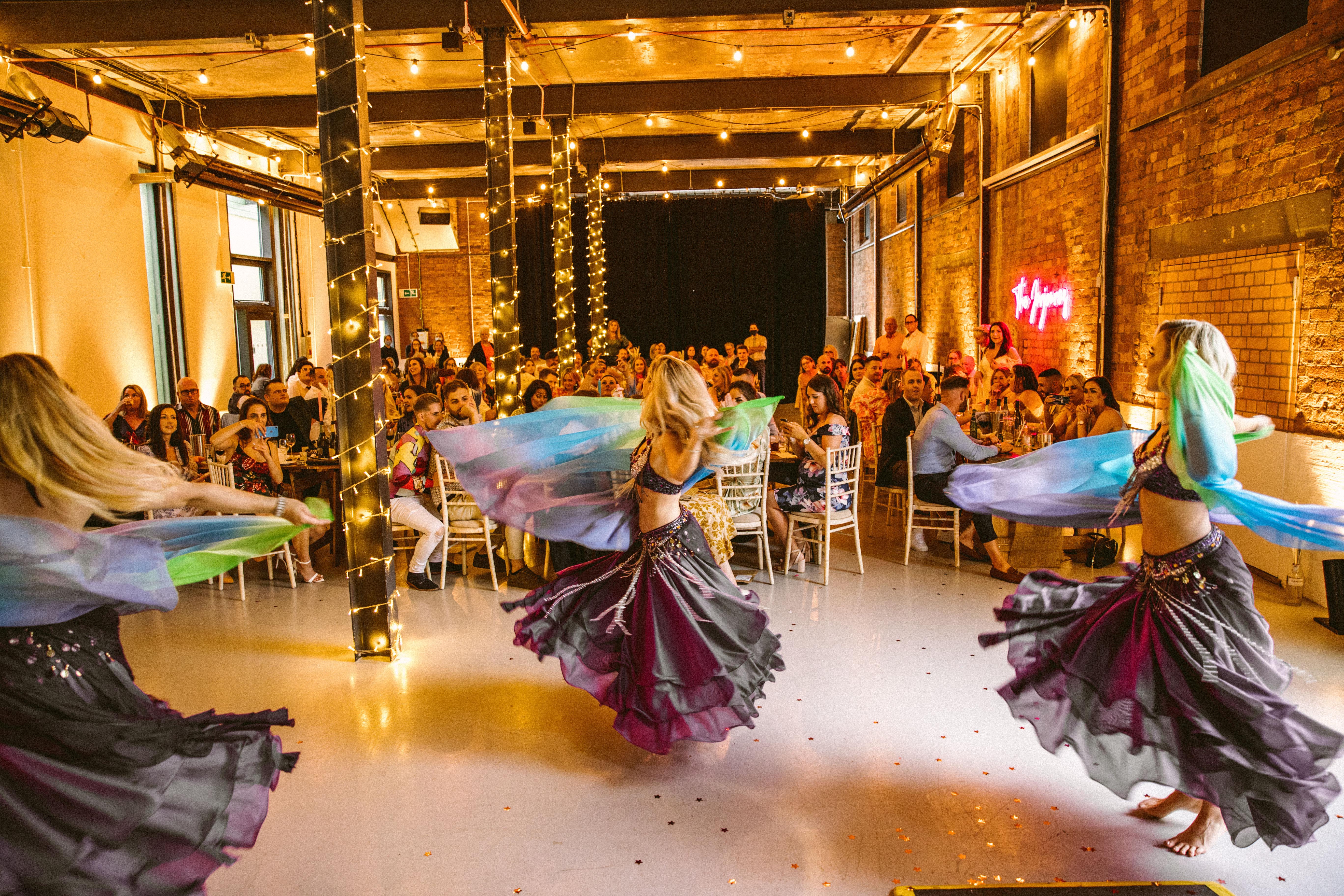 Vibrant dancers in flowing skirts twirl under warm, twinkling lights, captivating a lively audience seated at elegantly set tables.