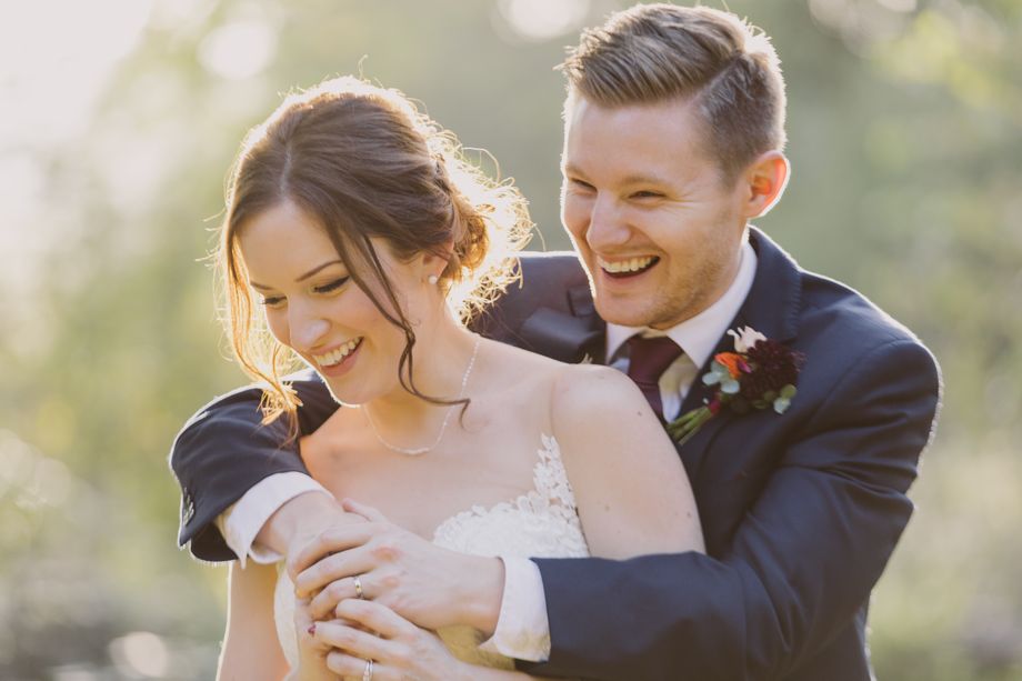A joyful couple embraces in soft, golden sunlight, surrounded by lush greenery, radiating love and happiness at their wedding celebration.