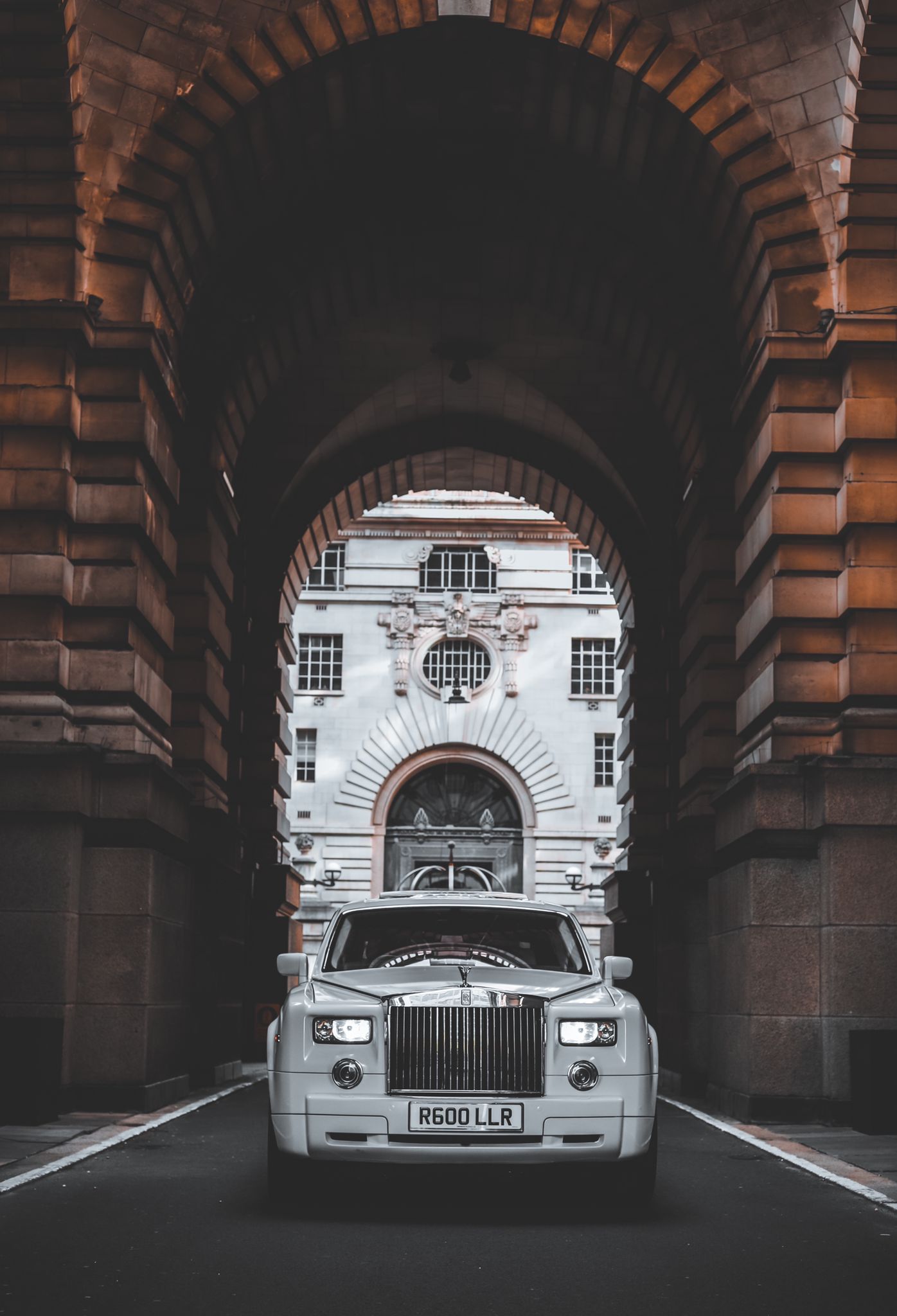A sleek white luxury car stands prominently beneath a grand archway, flanked by ornate stone columns. Dim lighting adds a sophisticated aura.