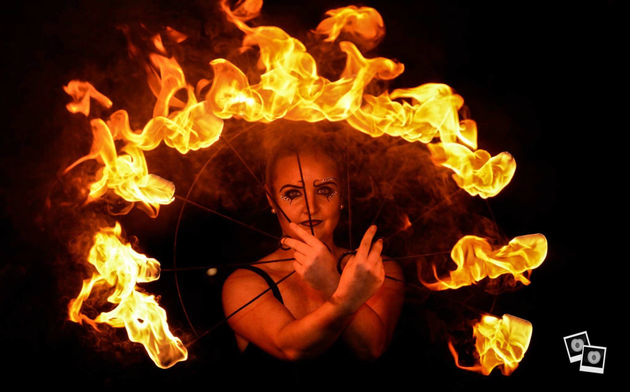 A performer skillfully spins flaming hoops against a dark backdrop, creating a dramatic atmosphere charged with energy and intensity.