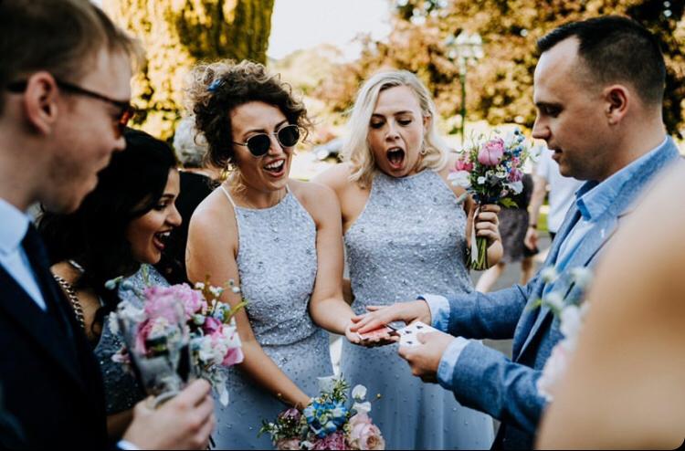 A joyful outdoor wedding scene showcases guests in shimmering, light blue dresses, laughter, and vibrant floral bouquets, capturing celebration.