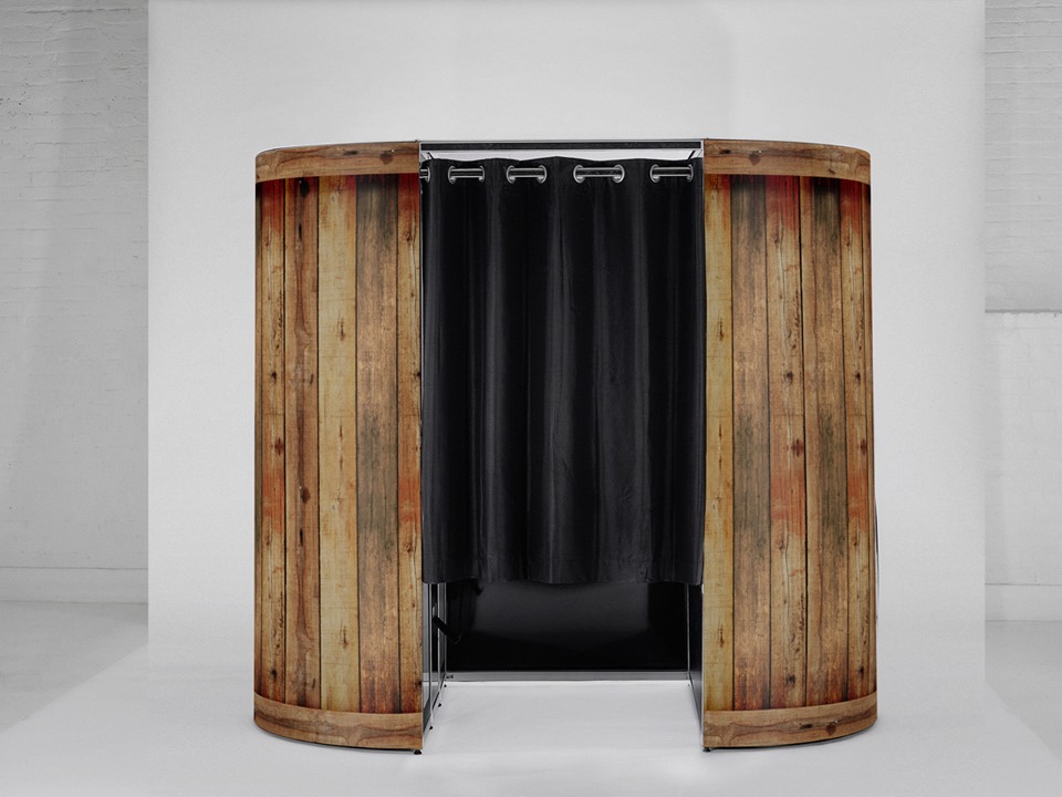 A rustic wooden shower stall features dark fabric curtains, set against a clean white backdrop, evoking a minimalist yet cozy atmosphere.