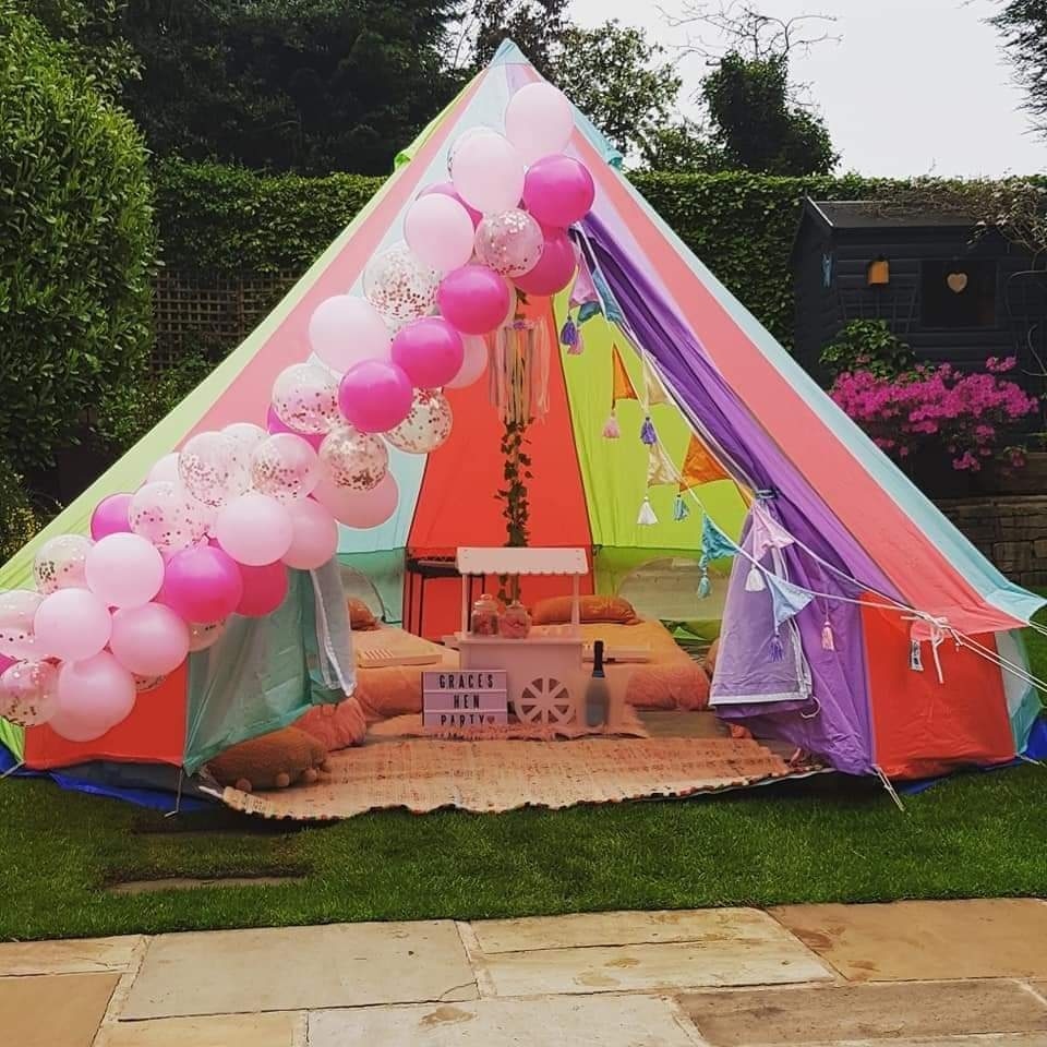 A vibrant tent features pink and pastel balloons cascading along the entrance, cozy cushions on a woven mat, creating a festive, playful atmosphere.