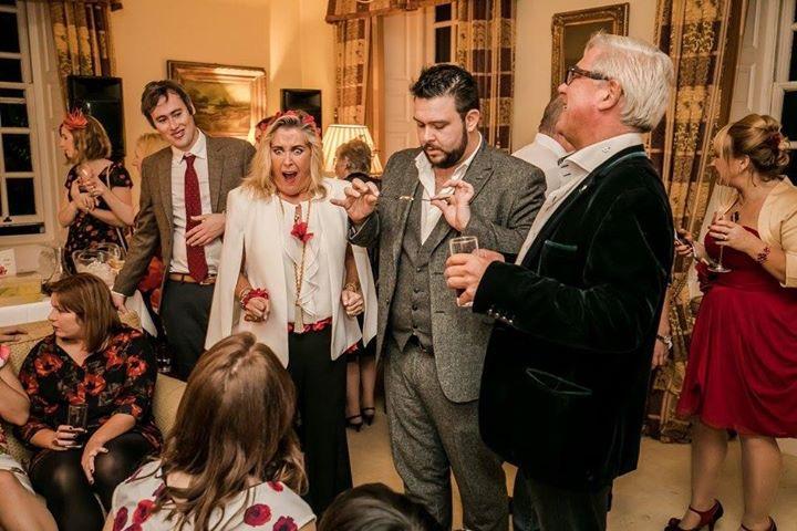 In a festive setting, guests in elegant attire enjoy drinks and laughter under warm lighting, creating a joyful, celebratory atmosphere.