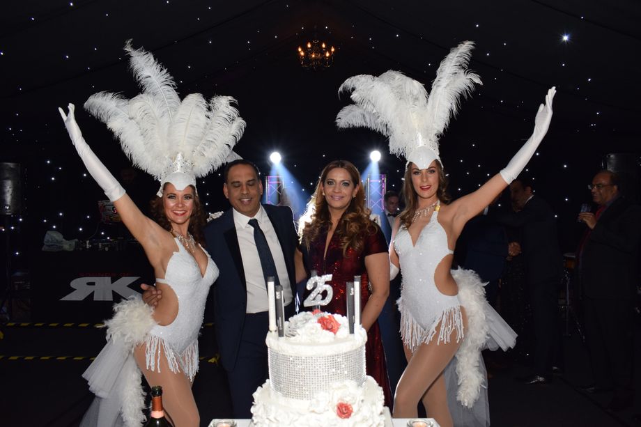 An elegantly decorated venue with soft spotlighting showcases a sparkling cake, while performers in white feathered outfits create a festive atmosphere.