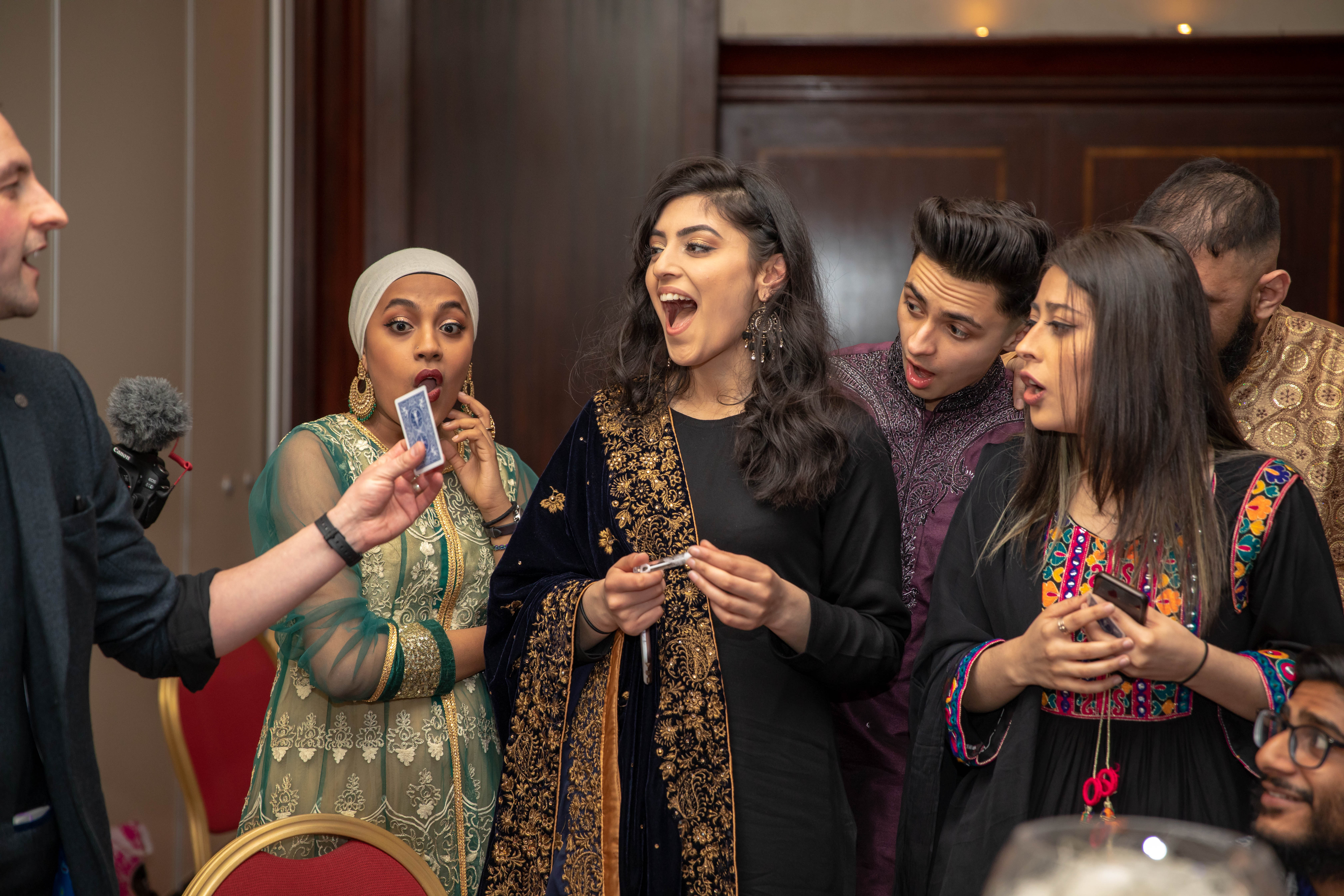 A group of four excited individuals in colorful traditional attire, gathering around a magician, showcasing vibrant patterns and atmosphere.