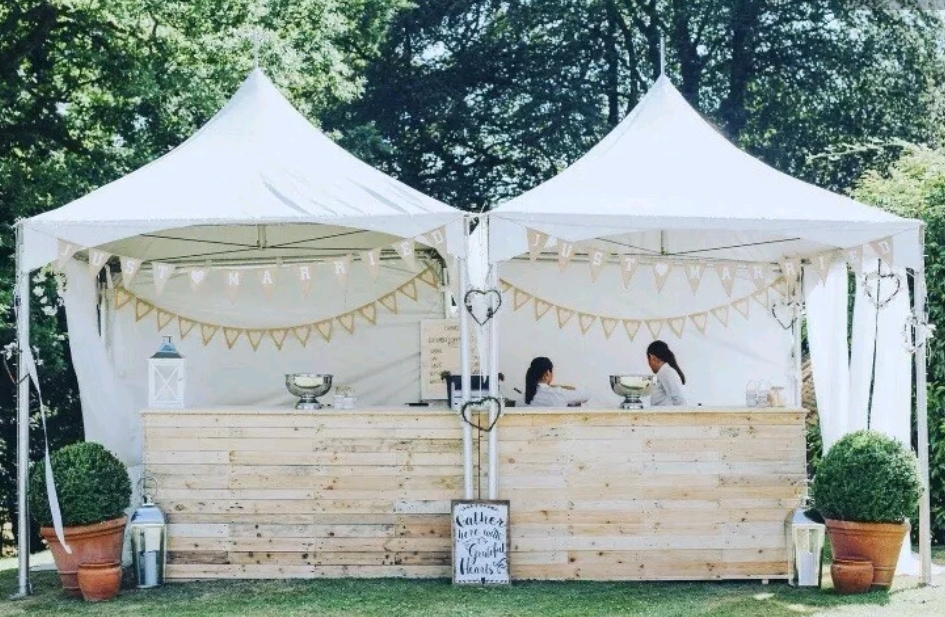 Two pristine white tents feature a rustic wooden bar, adorned with greenery and heart-shaped accents, creating a charming wedding atmosphere.