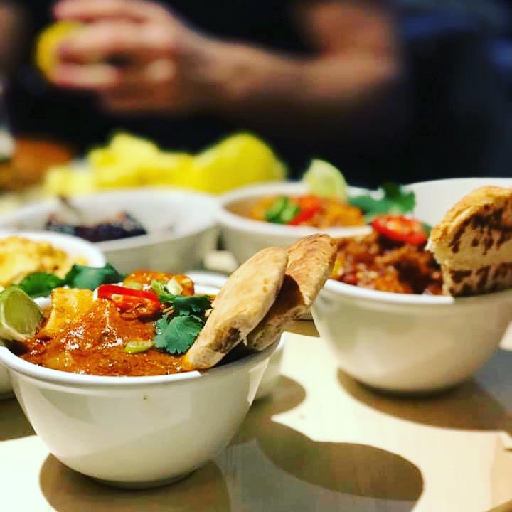 Colorful bowls of spiced curry, cilantro, and sliced chili are carefully arranged on a light wooden table, surrounded by warm, inviting lighting.