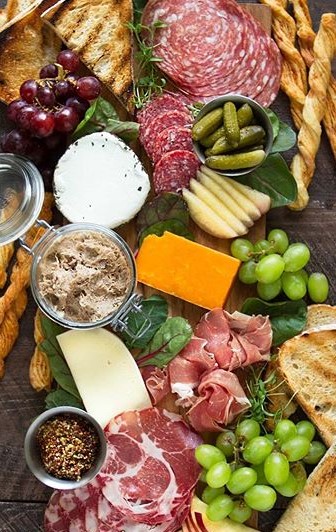 An artful spread featuring cured meats, cheeses, grapes, and crackers on a rustic wood board, enhanced by fresh greens and elegant presentation.