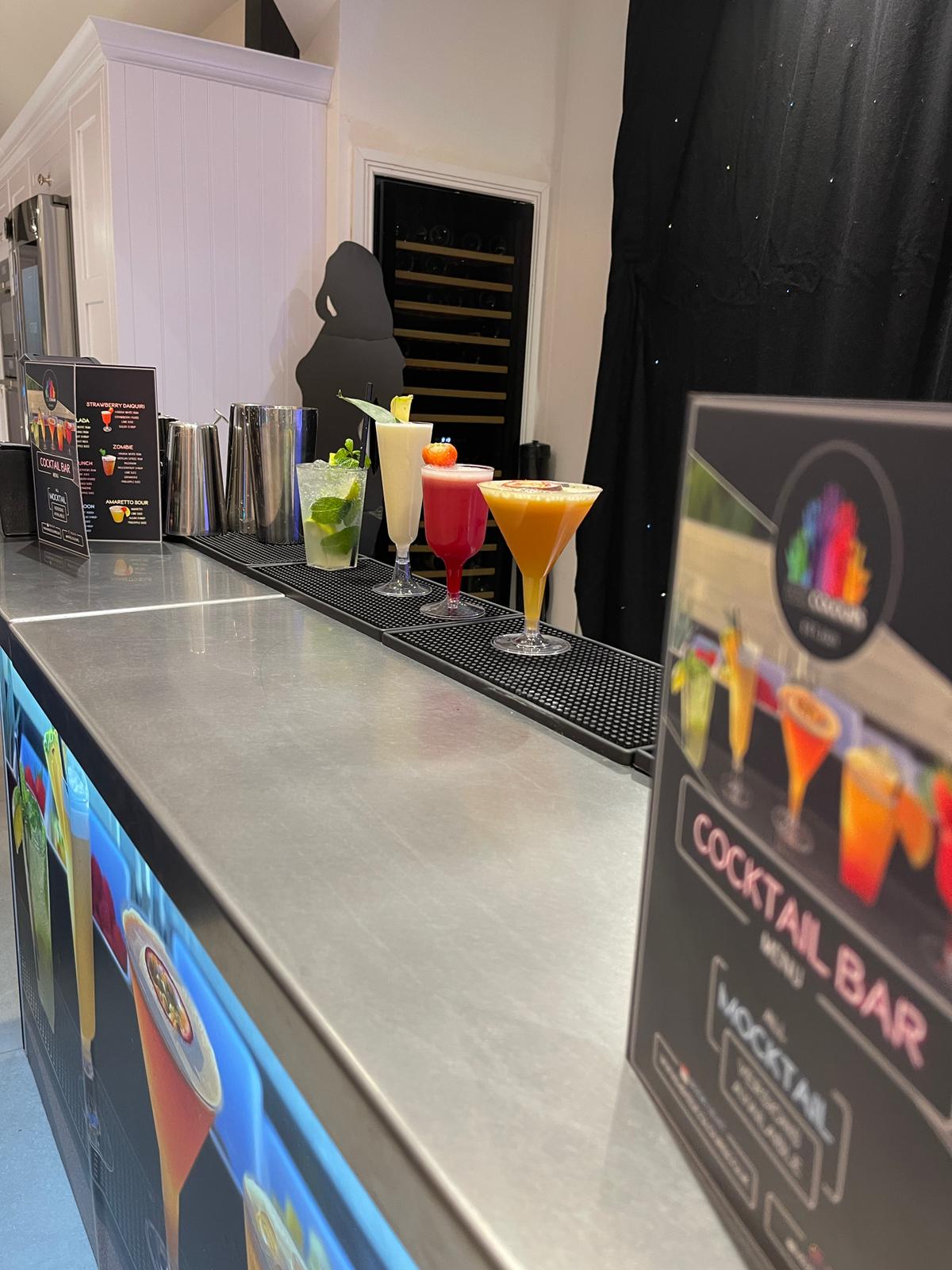 A polished stainless steel bar showcases vibrant cocktails in elegant glasses, arranged neatly, with a warm, inviting lighting ambiance.
