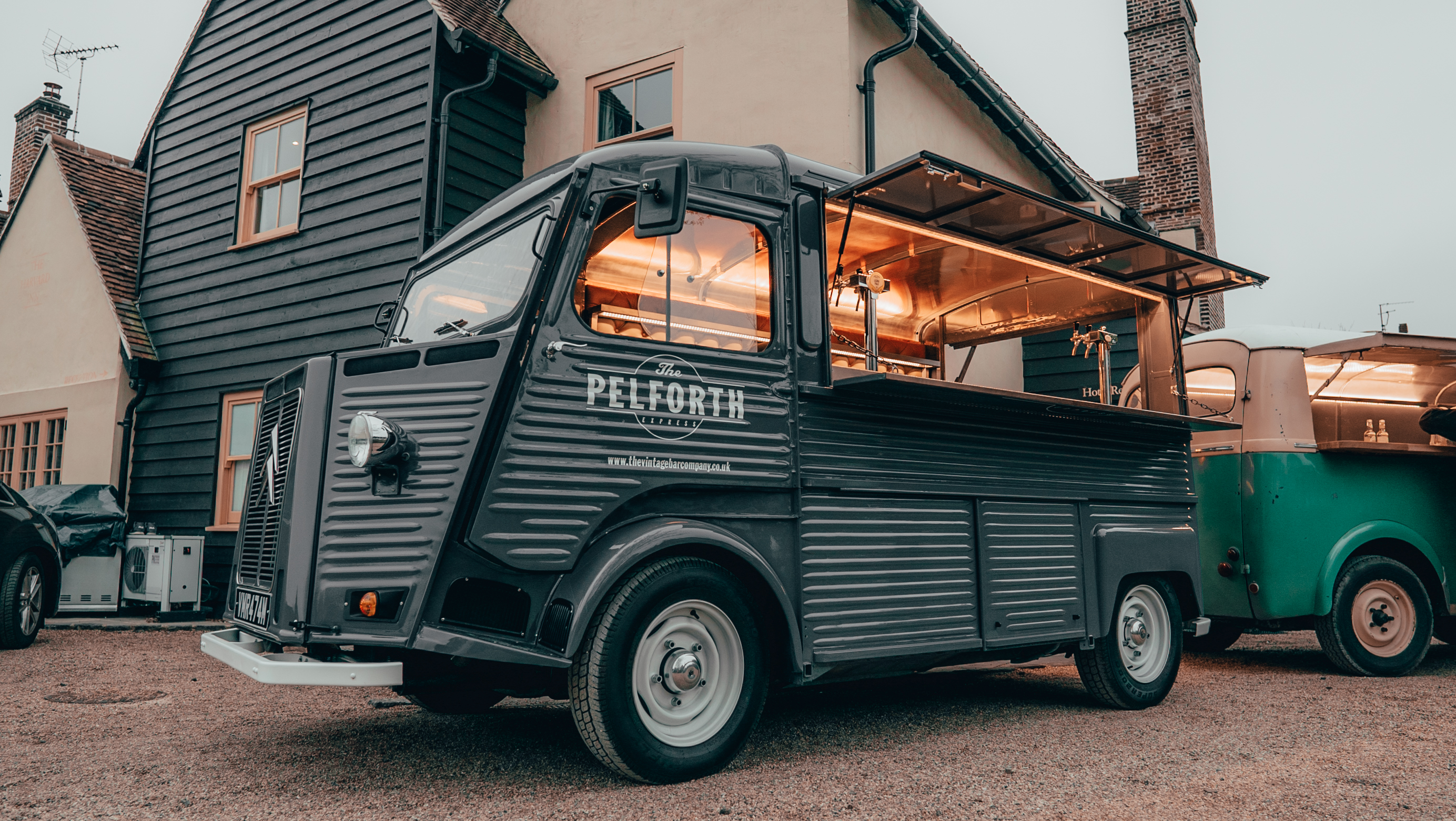 A vintage food truck with sleek gray metal, featuring a glass serving area, parked near a cozy home, radiates a welcoming atmosphere.