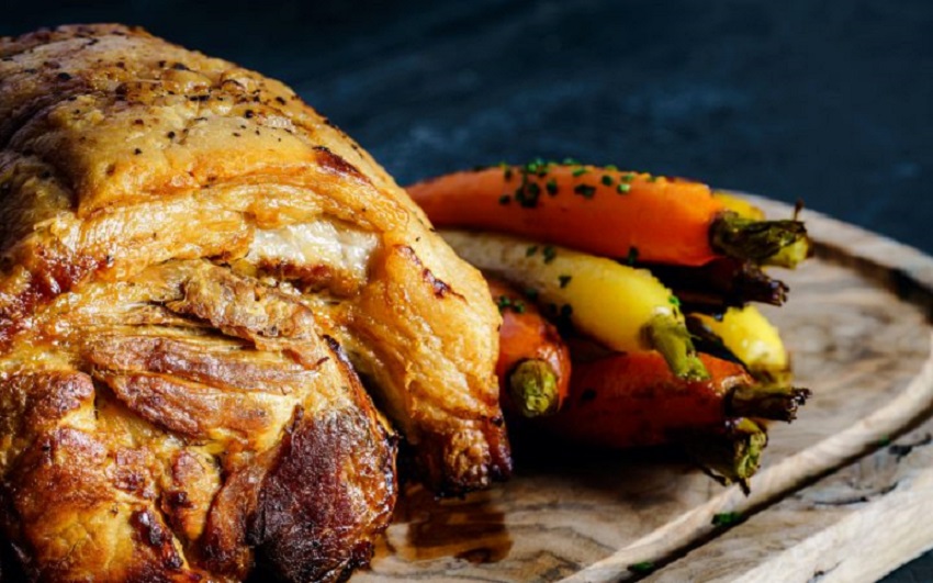 A succulent roast, golden-brown and crispy, pairs beautifully with vibrant carrots, elegantly plated on a rustic wooden board, exuding warmth.